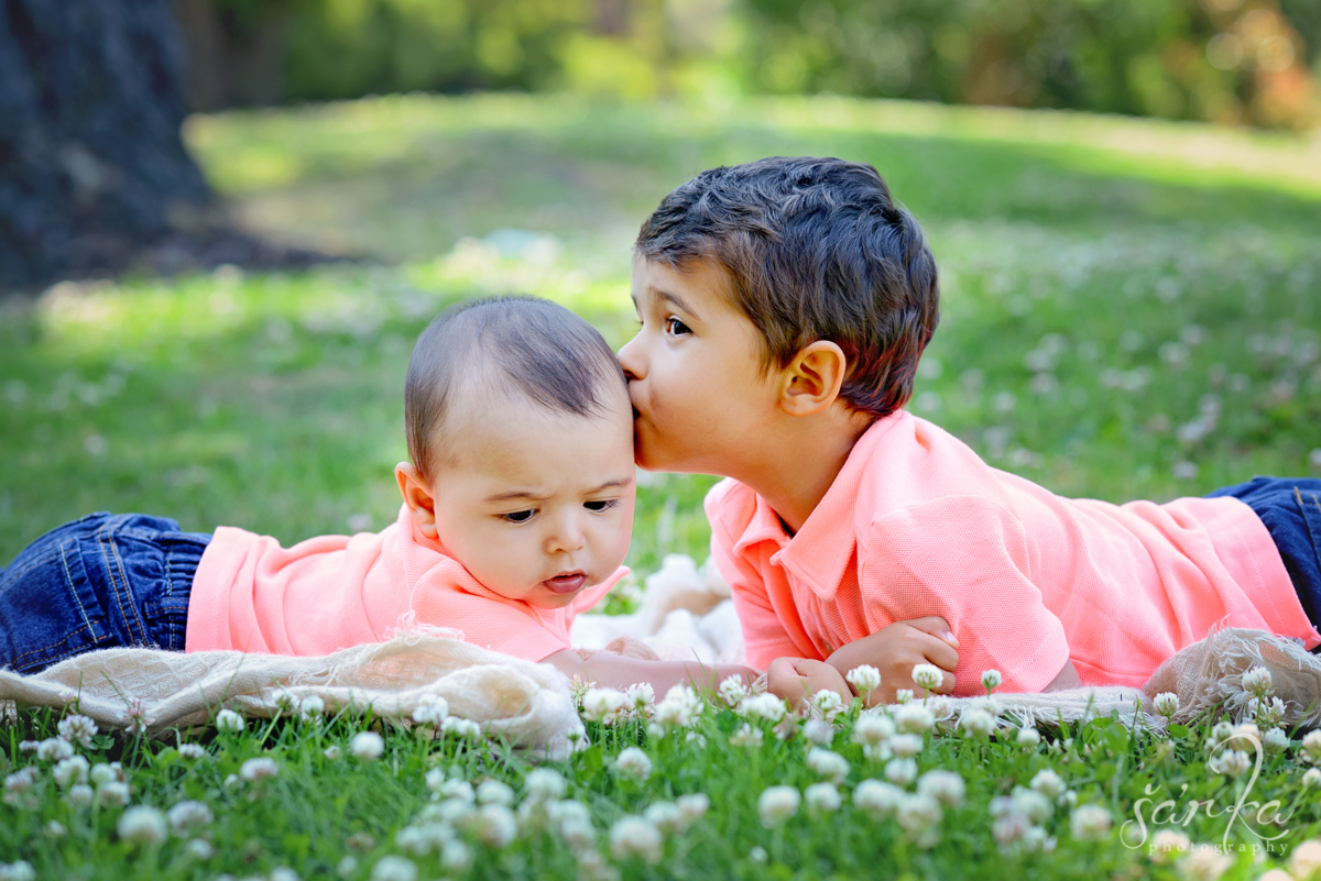 older brother kissing his 6 months old brother laying in the grass photographed by San Francisco Baby and children photographer Sarka Photography