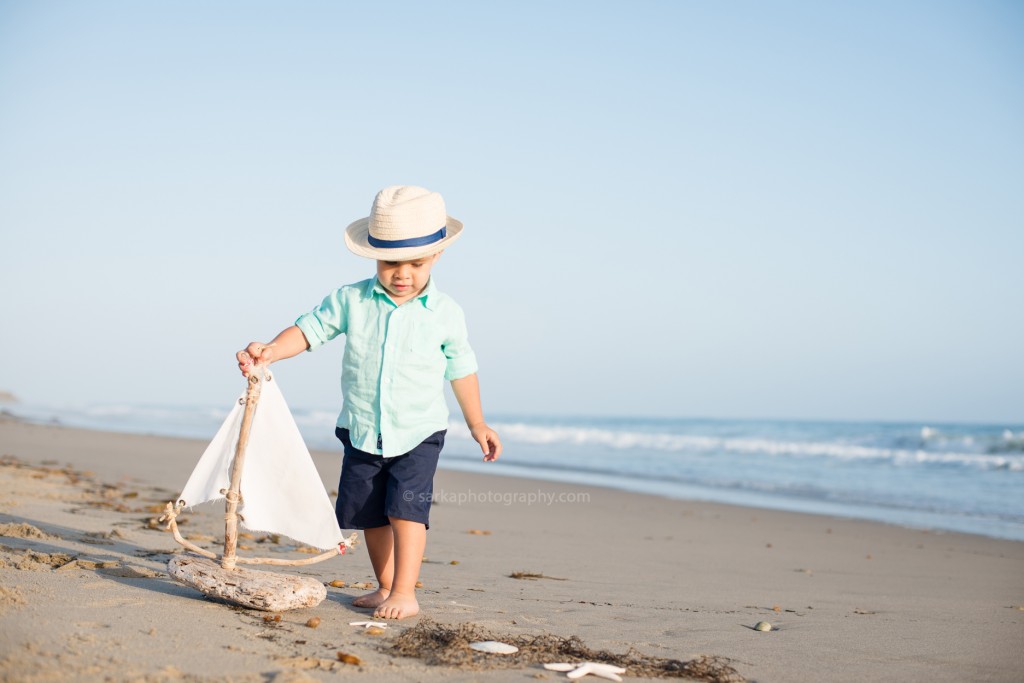 toddler boy playing with a driftwood boat on the beach photographed by Santa Barbara children photographer Sarka Photography