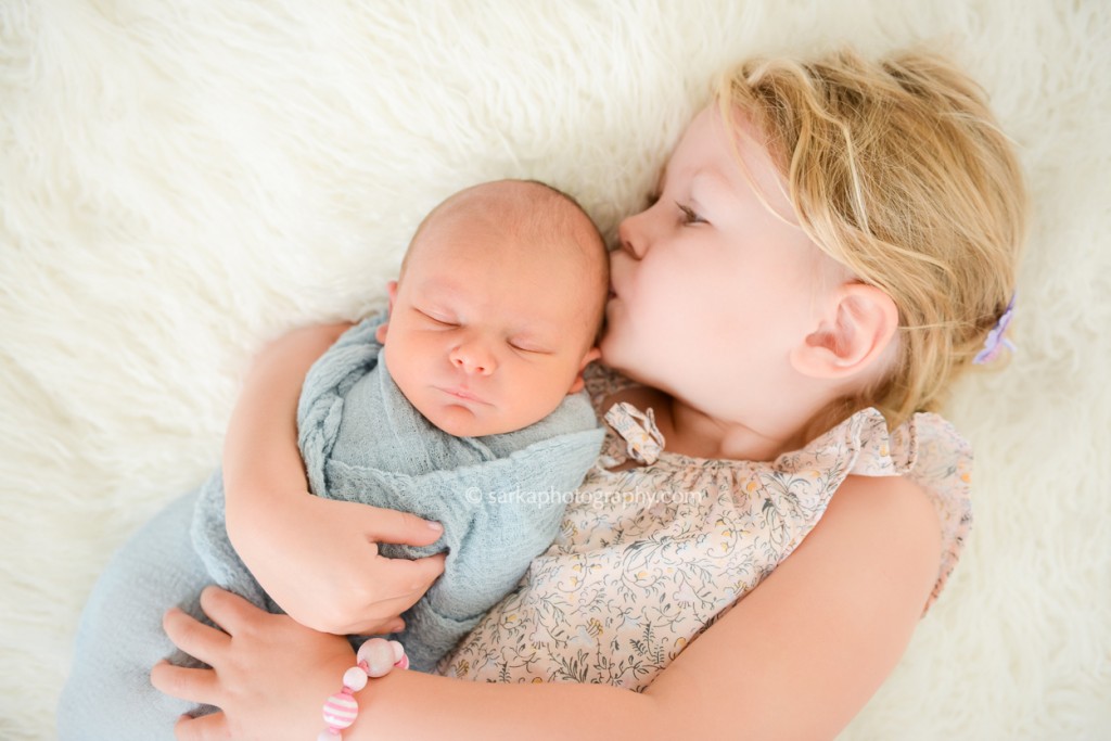 toddler girl holding and kissing her newborn brother photographed by San Francisco and Santa Barbara baby photographer Sarka Photography