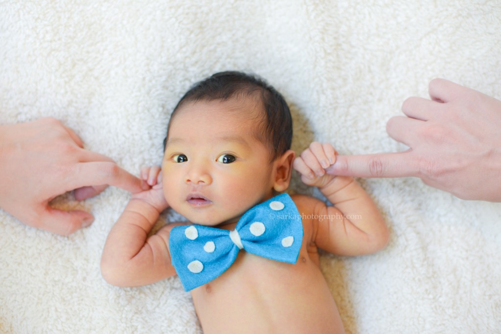 newborn baby boy with bowtie holding his parents fingers photographed by San Francisco East Bay Area baby photographer Sarka Photography