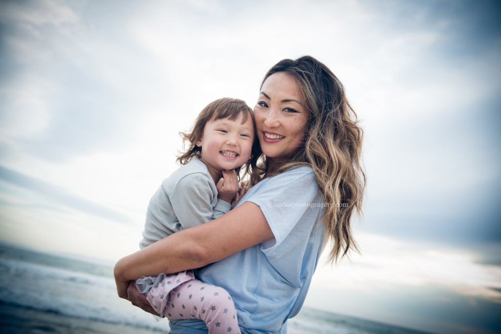 young mom holding her daughter on the beach little girl in her moms arms on the beach at sunset photographed by Santa Barbara children and family photographer by Sarka Photography