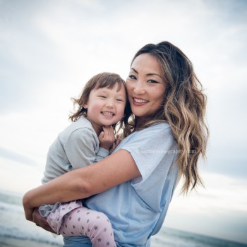 young mom holding her daughter on the beach little girl in her moms arms on the beach at sunset photographed by Santa Barbara children and family photographer by Sarka Photography