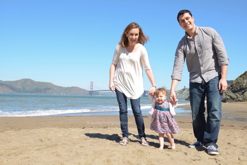 young parents holding walking on the beach in San Francisco with their one year old baby girl photographed by San Francisco and Santa Barbara baby photographer Sarka