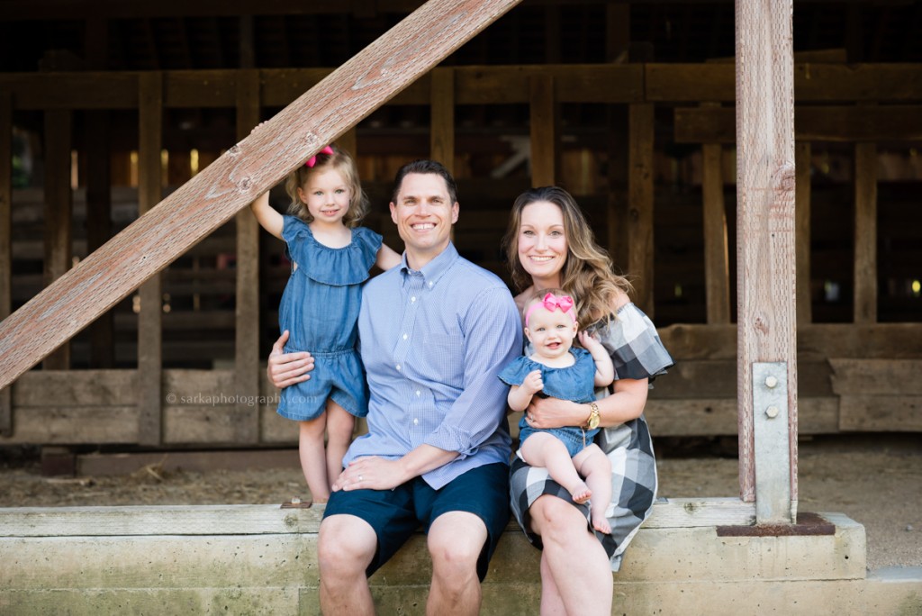 family with two children sitting at a barn during their family photo session with Sarkaphotography 