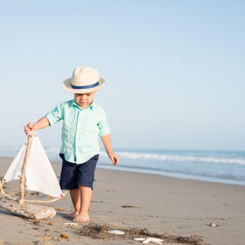 toddler boy walking on a beach with a driftwood boat during his child portrait lifestyle photo session in Carpinteria by Santa Barbara children and family photographer sarkaphotography