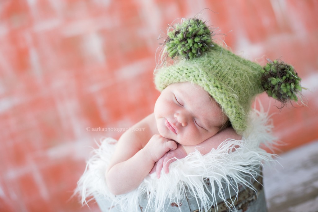 newborn sleeping in a vintage bucket wearing a hand knitted hat photographed by sarka photography 