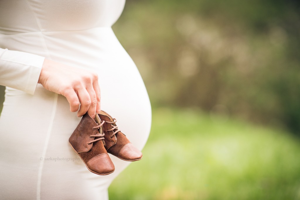 expecting mother holding baby shoes during her maternity photo session portrait in Santa Barbara photographed by sarkaphotography