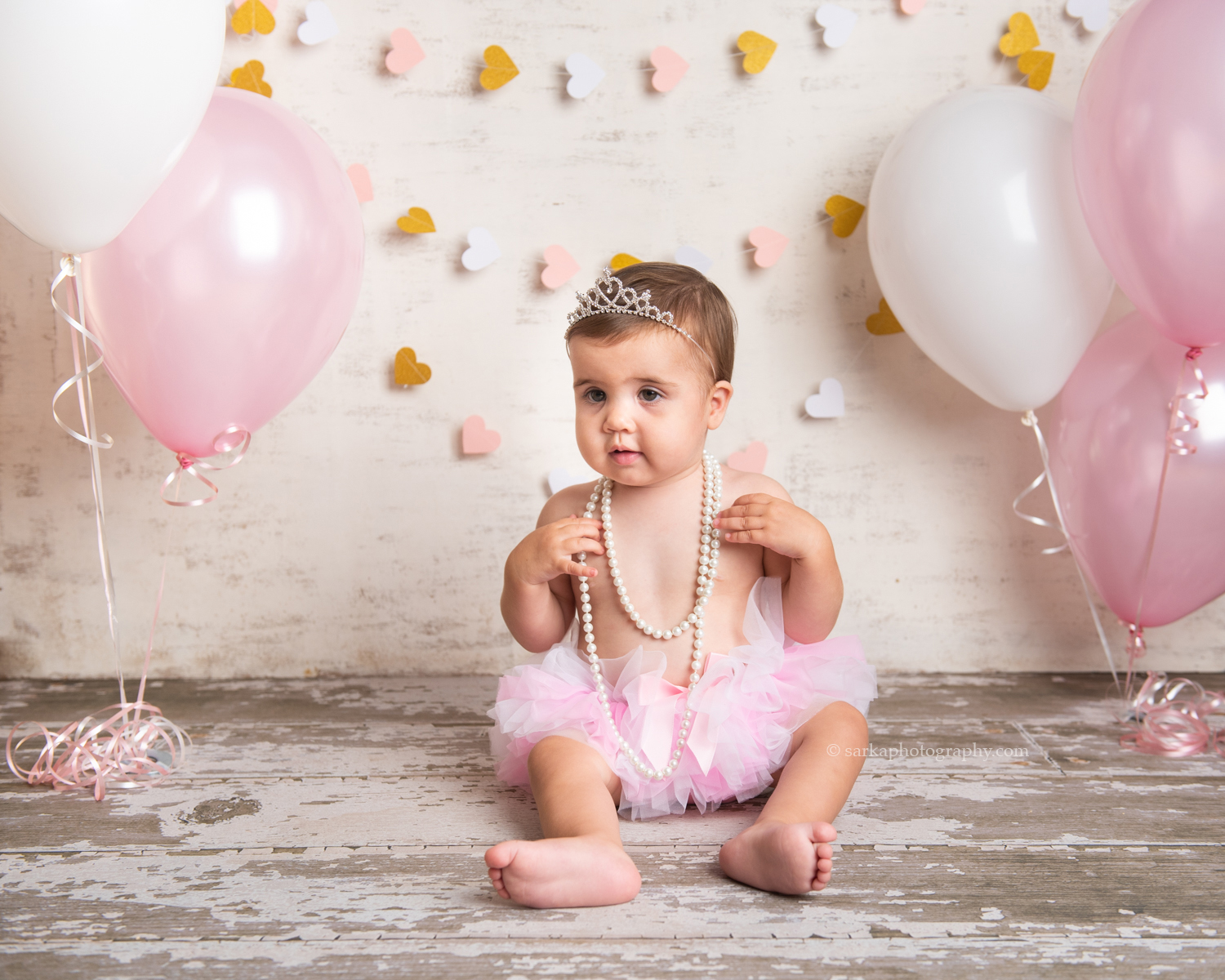 one year old baby girl playing with pearls during her one year old cake smash photo session by sarkaphotography in Santa Barbara
