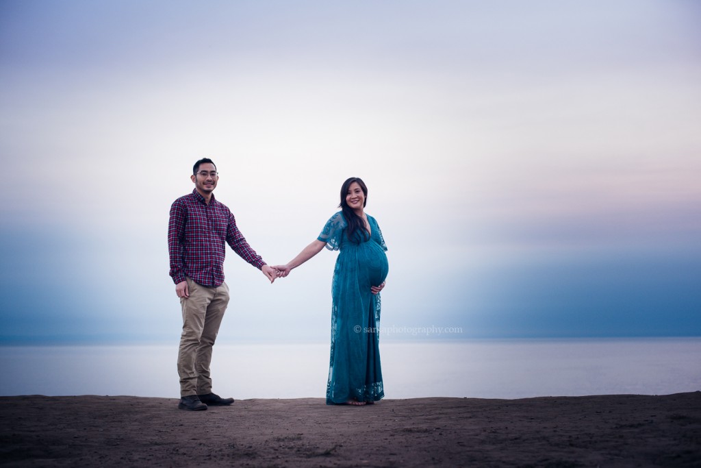expecting couple standing above the ocean at sunset during their pregnancy photo session in Santa Barbara