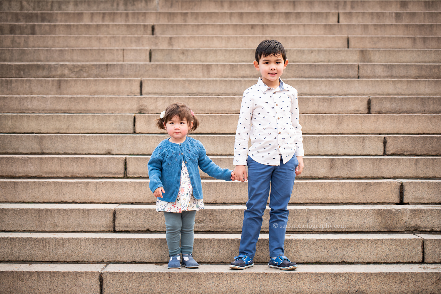 children holding hands on a staircase during their family photo session in Central Park New York