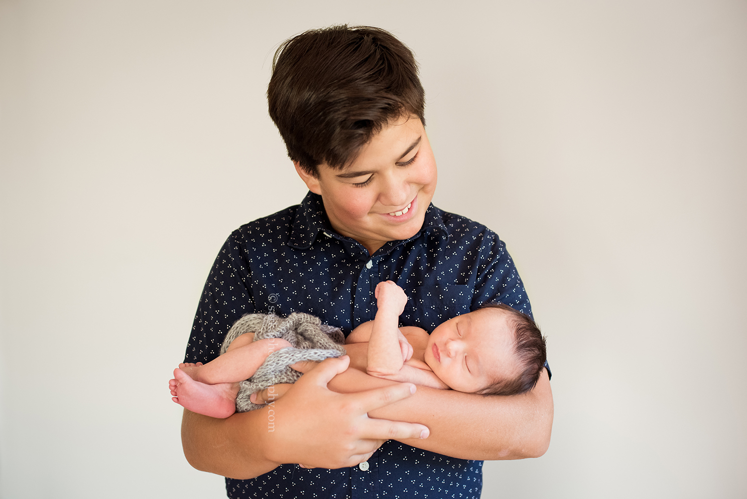 older brother holding his newborn brother in his arm during his family photo session in Santa Barbara