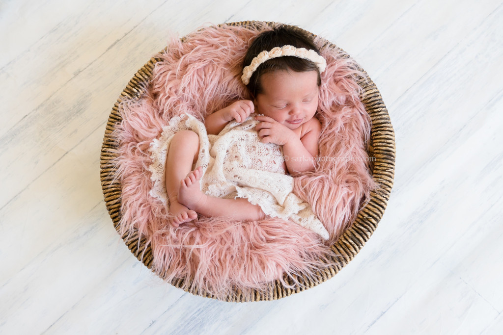 newborn baby girl smiling while sleeping in a vintage basket during her baby photos in Carpinteria