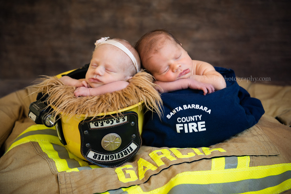 newborn twins sleeping in a firefighter helmet uniform during their newborn photo session in Santa Barbara